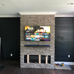 TV mounted on a stacked-stone fireplace beside a black shiplap accent wall